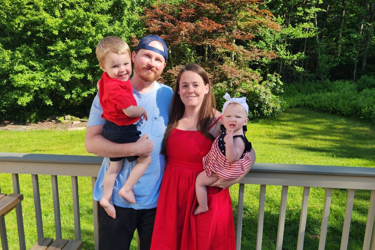 Мужчина и женщина стоят на деревянной террасе с мальчиком и девочкой в ​​окружении зелени и деревьев в солнечный день.