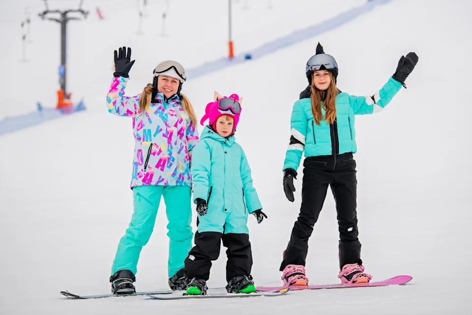 семья с детьми катается на сноуборде на склоне горнолыжного курорта. Зимние виды спорта и развлечения на свежем воздухе.