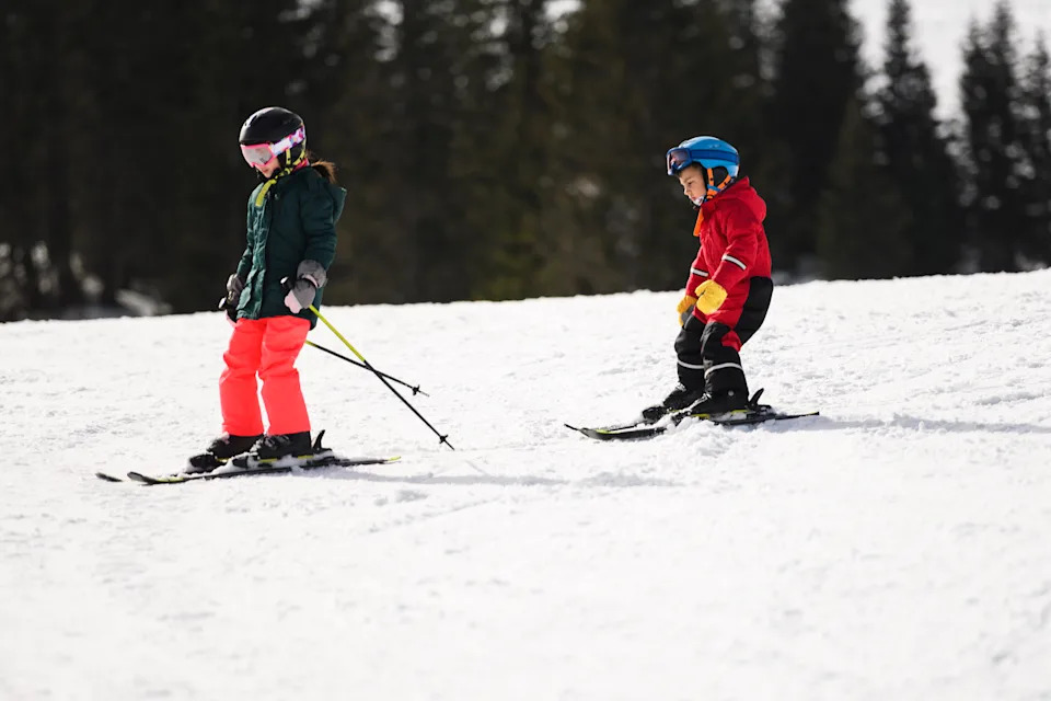 Два юных лыжника наслаждаются солнечным днем ​​на склонах, практикуя свои навыки катания на свежем снегу.