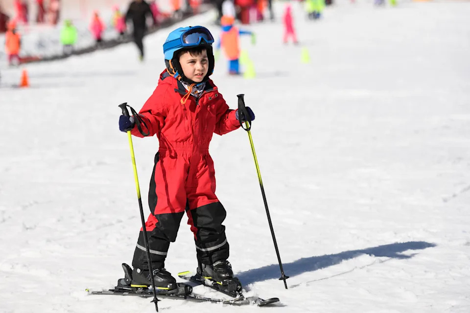 Мальчик учится кататься на лыжах в солнечный зимний день, наслаждаясь заснеженным склоном горы и свежим воздухом