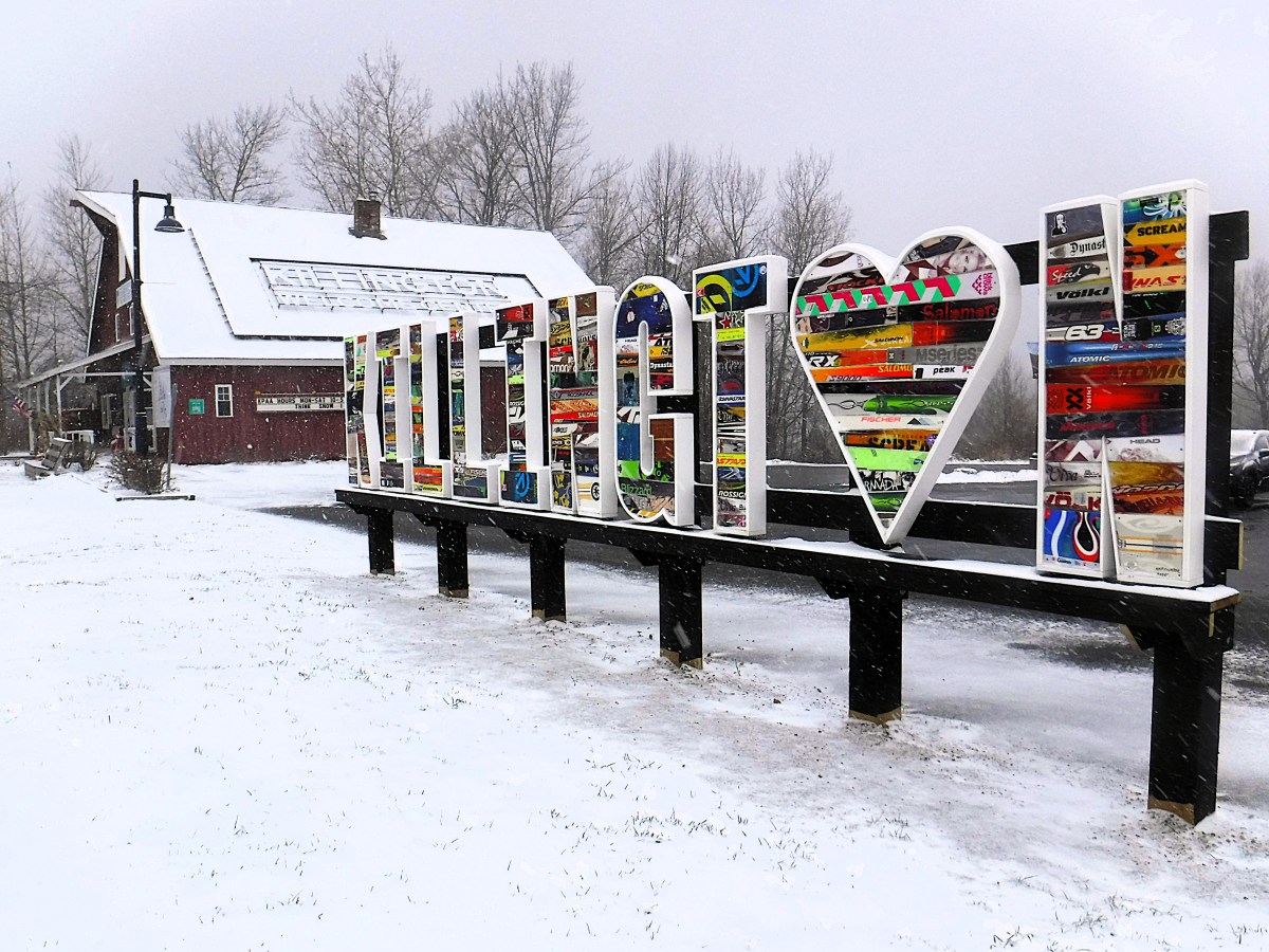Большой уличный знак с надписью "Я (сердце) ВТ" сделанные из лыж стоят перед красным зданием в снежный пасмурный день.