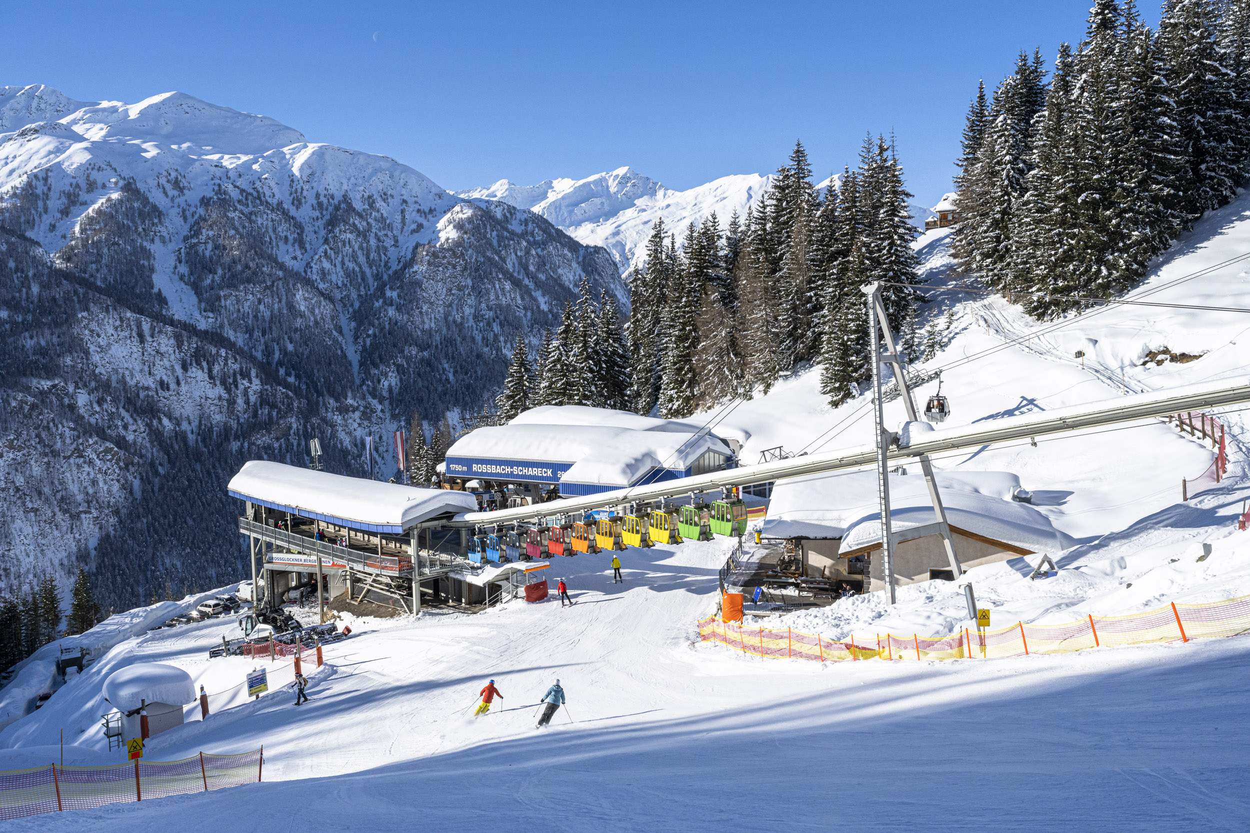 Лыжники на солнечном склоне в Хайлигенблут-ам-Гроссглокнере с гондольным подъемником и заснеженными горами.
