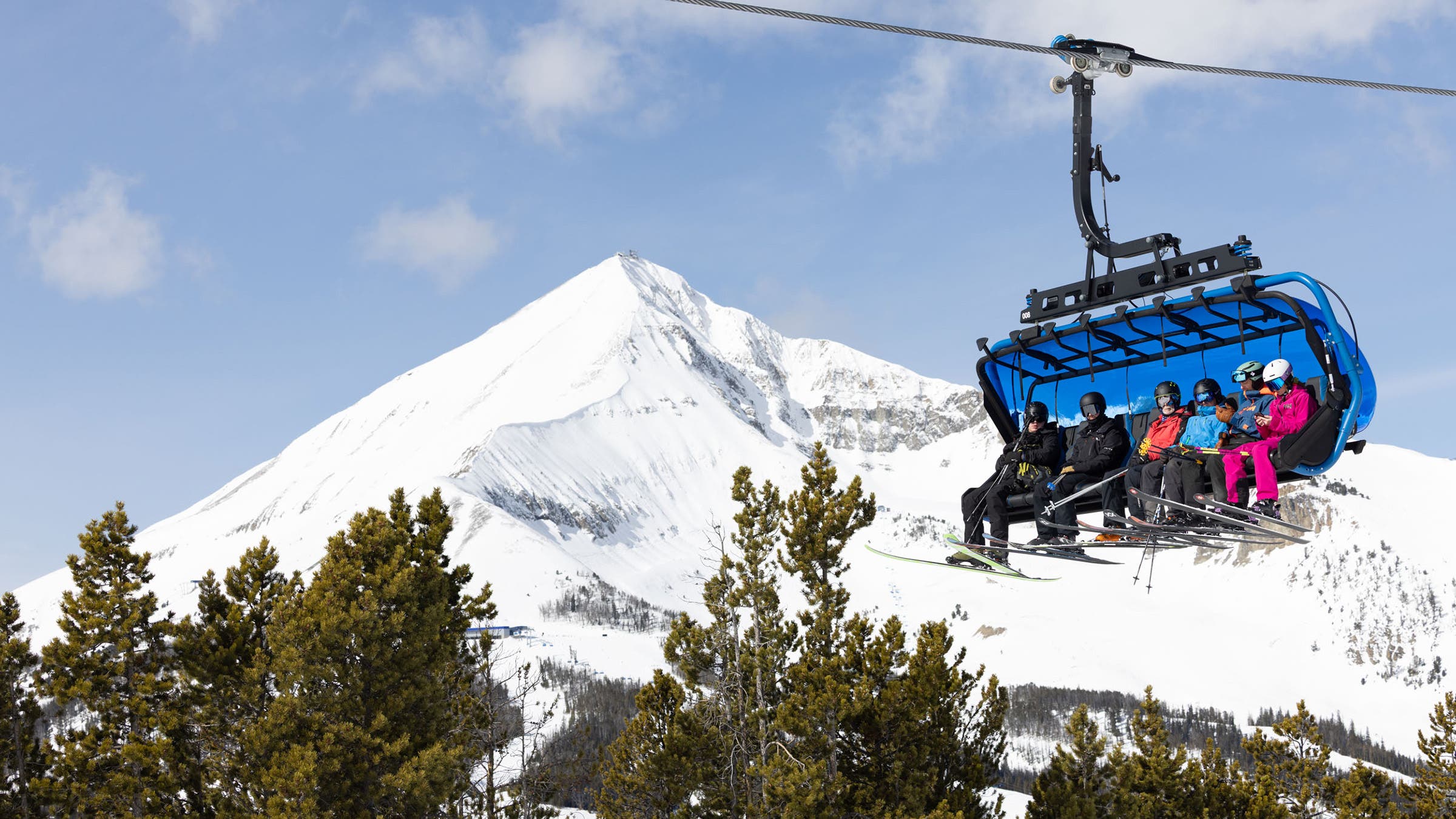 Лыжники на 8-местном кресельном подъемнике на курорте Big Sky Resort, Лоун-Пик, на заднем плане
