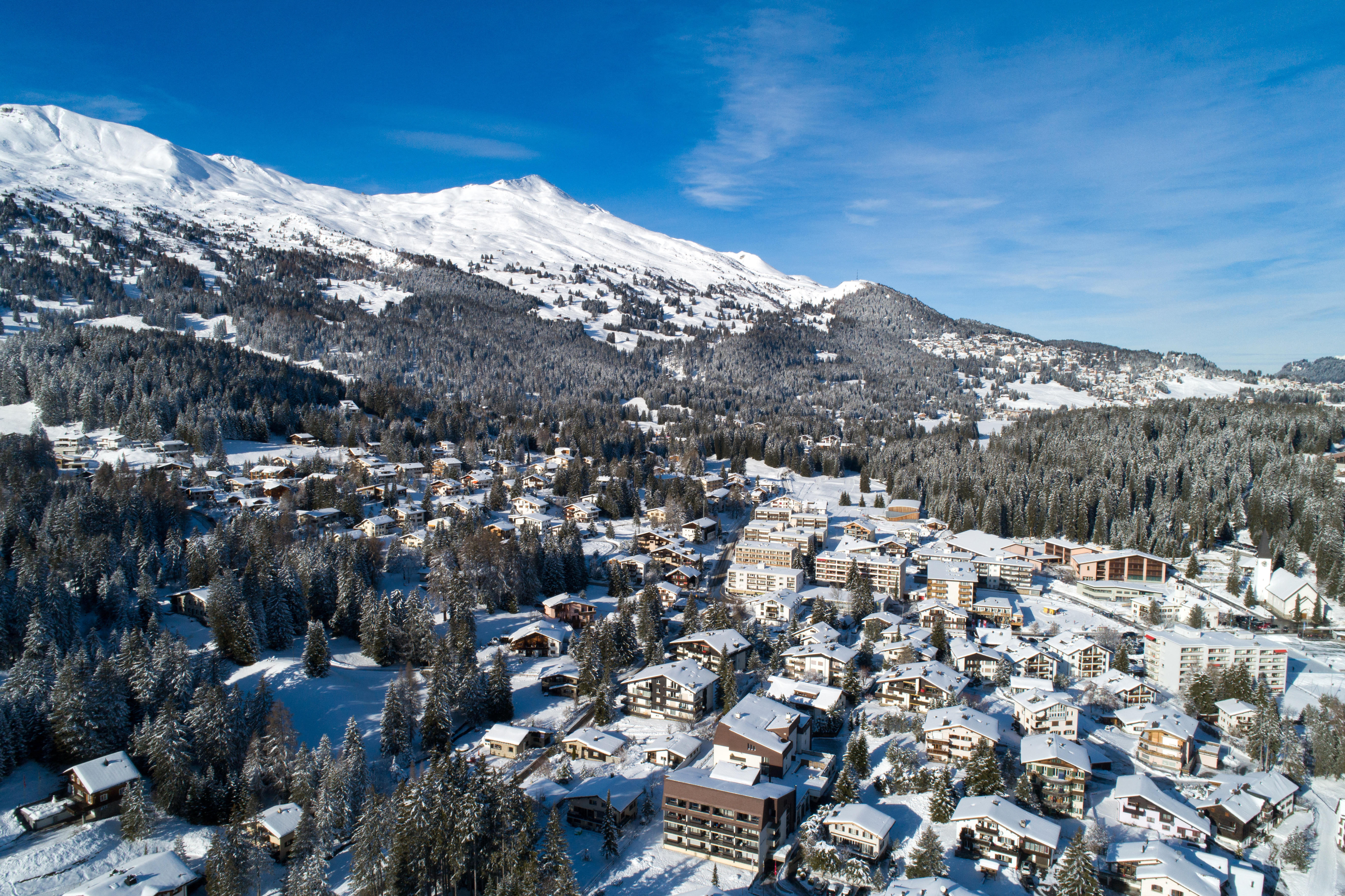 Вид с воздуха на Ленцерхайде-Ваз зимой с заснеженными горами, соснами и зданиями.